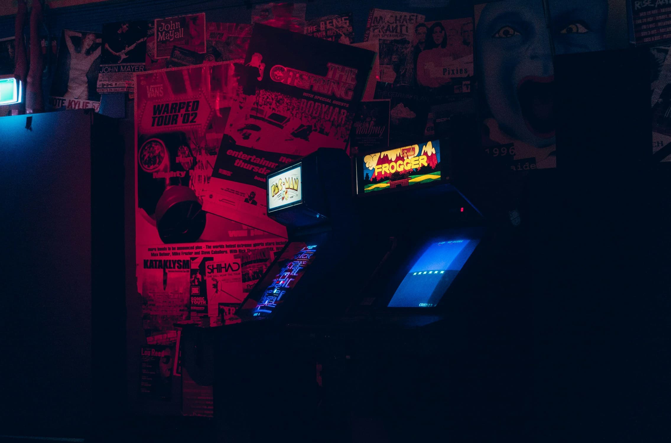 Classic Pac-Man and Frogger arcade cabinets glowing under neon lights at Vybez Arcade